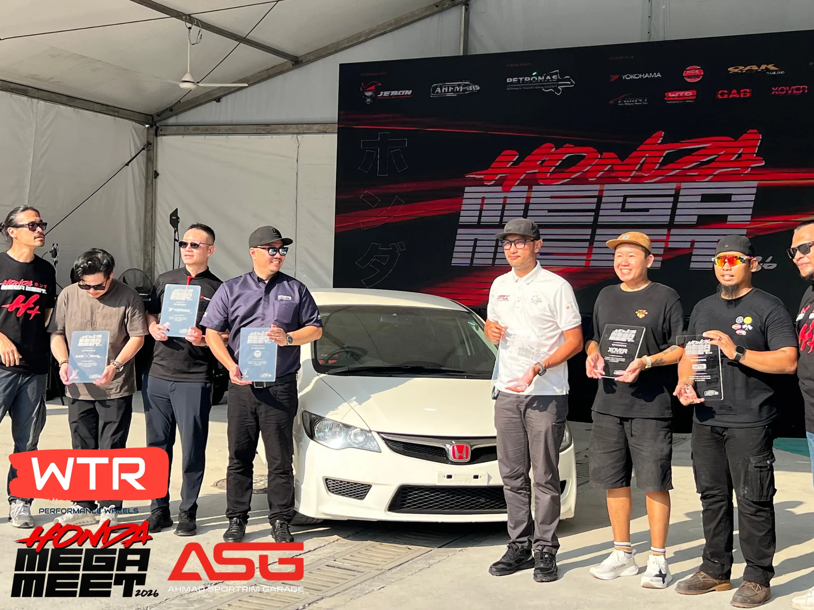 Award recipients gathered around a white Honda at a community event
