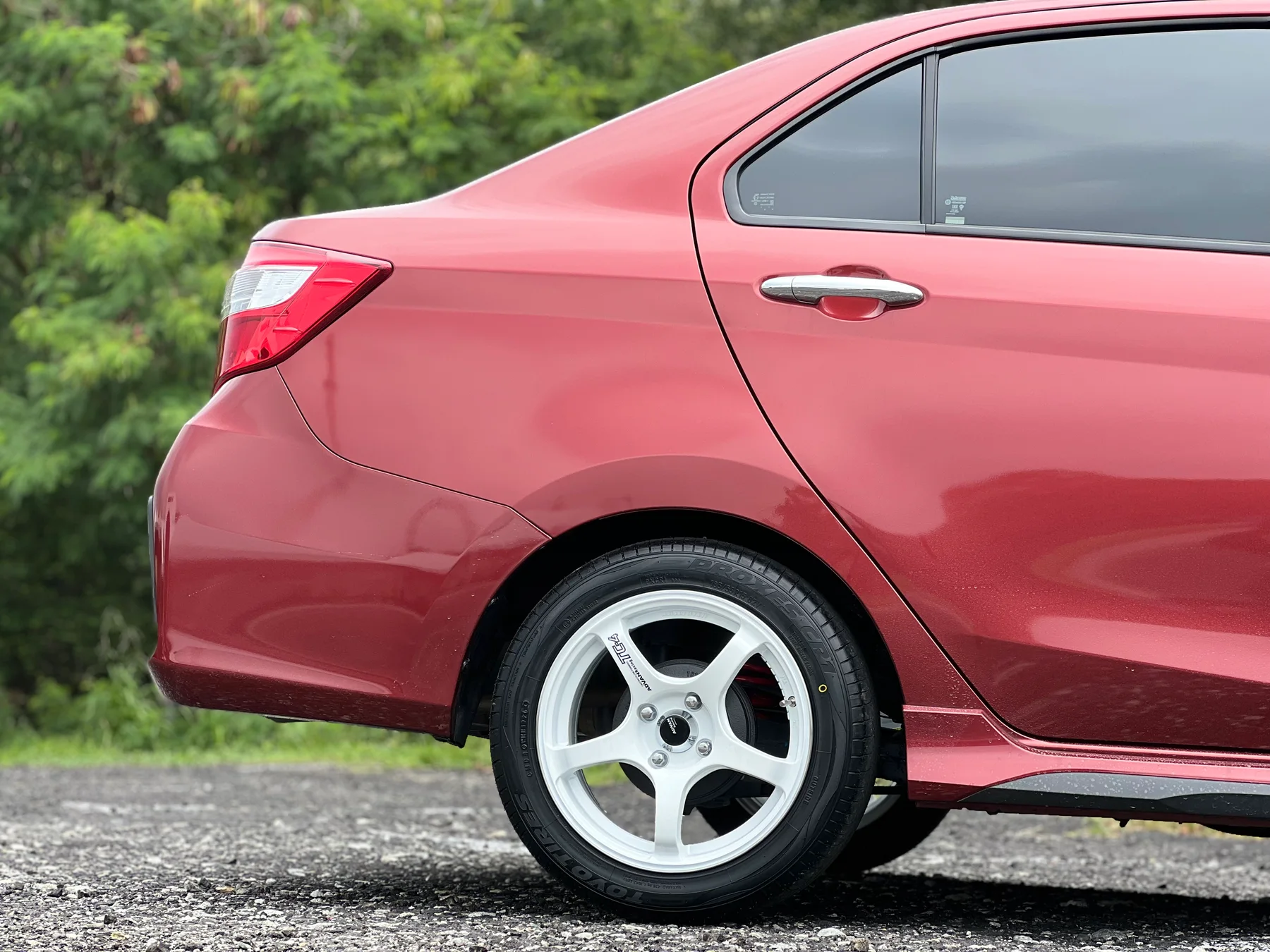 Red Perodua Bezza rear side view with white five-spoke wheels