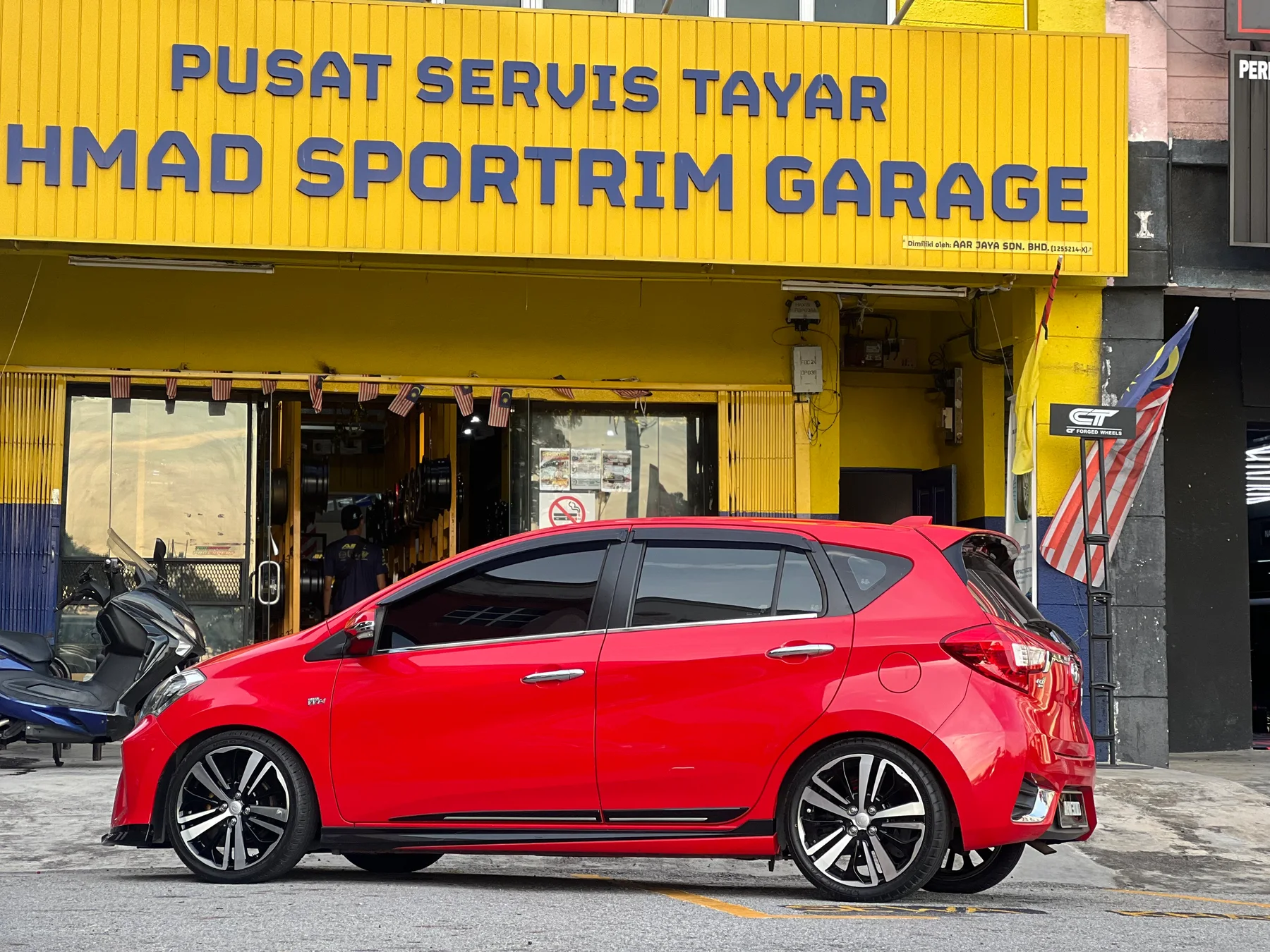 Red Perodua Myvi side profile with dark sport wheels outside ASG